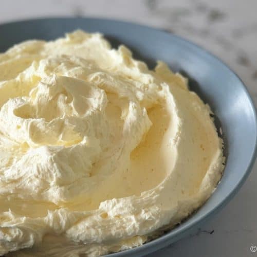 pale yellow buttercream icing swirled in a blue grey bowl on marble background